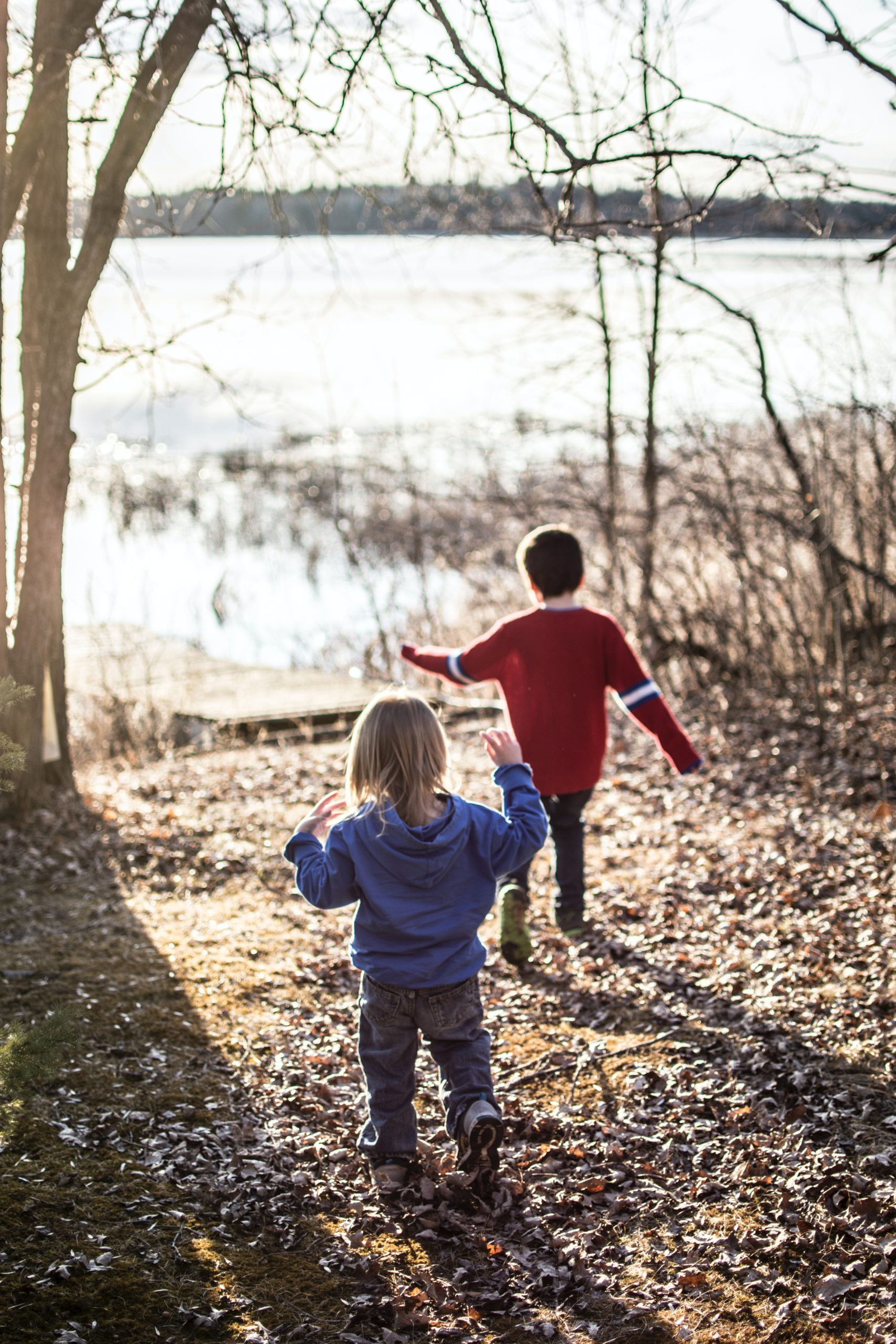 Two small children playing in the leaves outside while wearing sweaters